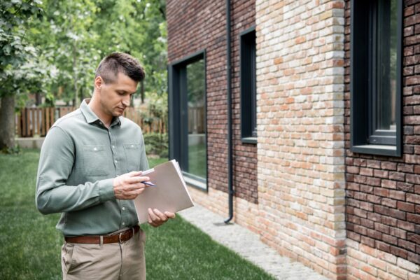 real estate agent holding folder and pen while standing near contemporary building on city street real estate agent holding folder and pen while standing near contemporary building on city street